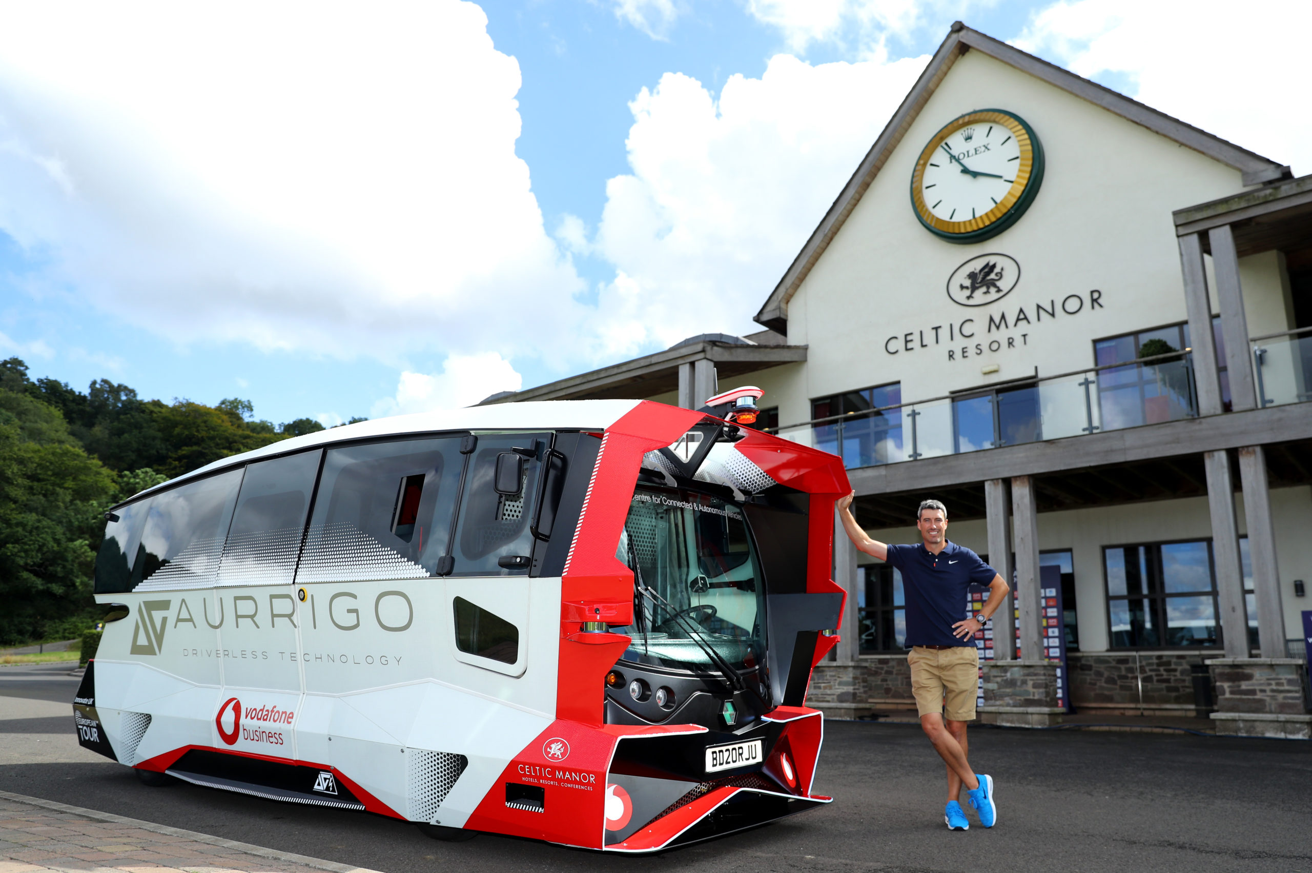 European Tour Pro Golfer Ross Fisher stands next to the Aurrigo x Vodafone Driverless Shuttle